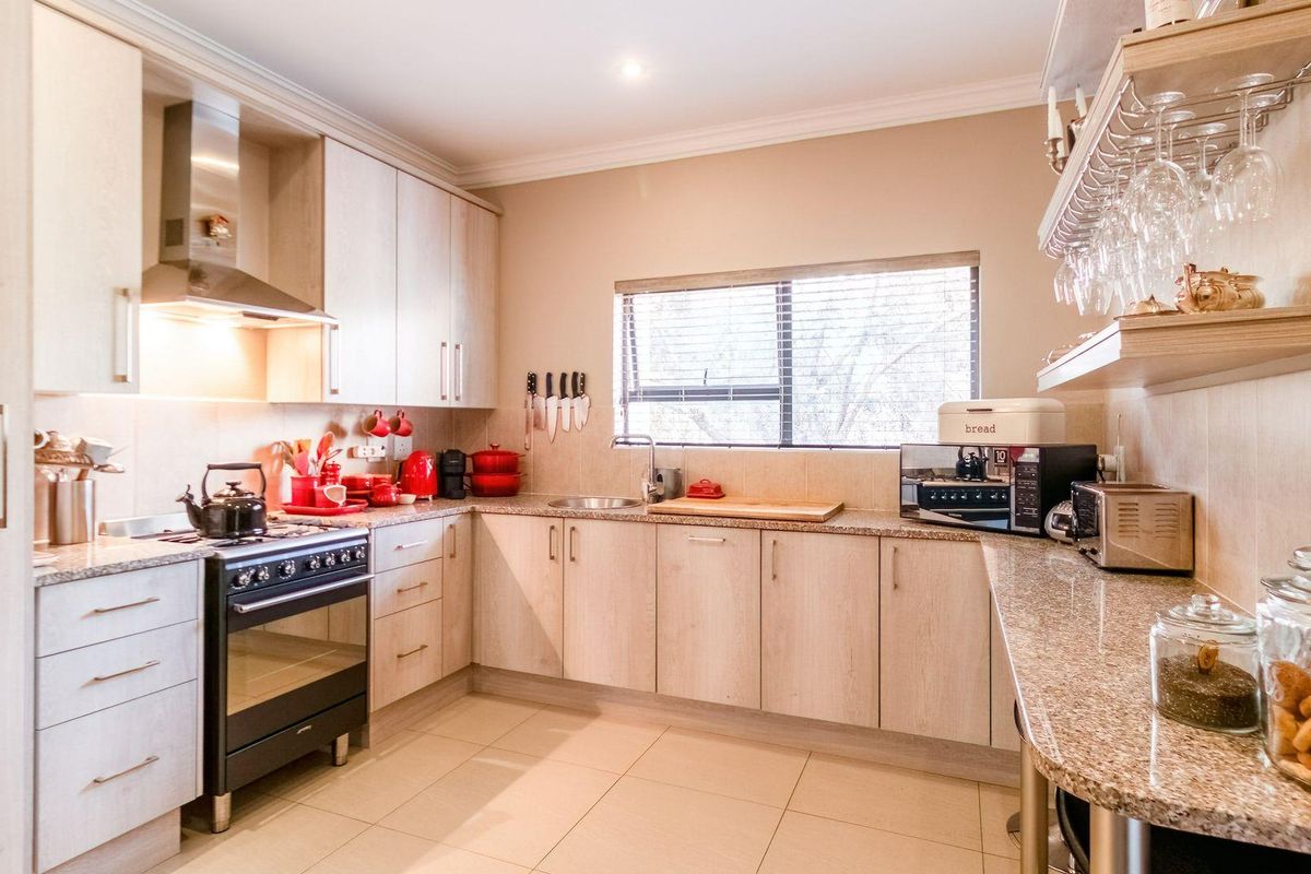 A functional kitchen featuring light wood cabinetry, granite countertops, a stainless steel extractor fan, and a freestanding gas stove.