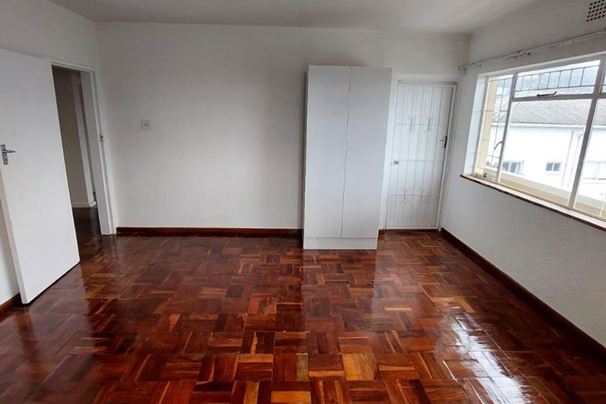 A bright, empty bedroom featuring polished parquet flooring, a built-in wardrobe, and a security gate on the door.