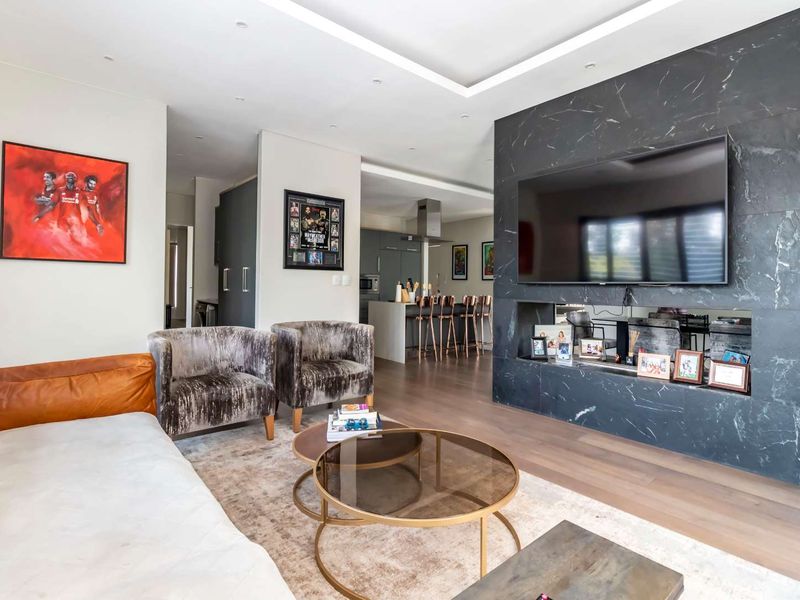 Spacious open-plan living area featuring a striking marble fireplace wall, recessed ceiling lighting, and seamless flow into a modern kitchen with a central island.