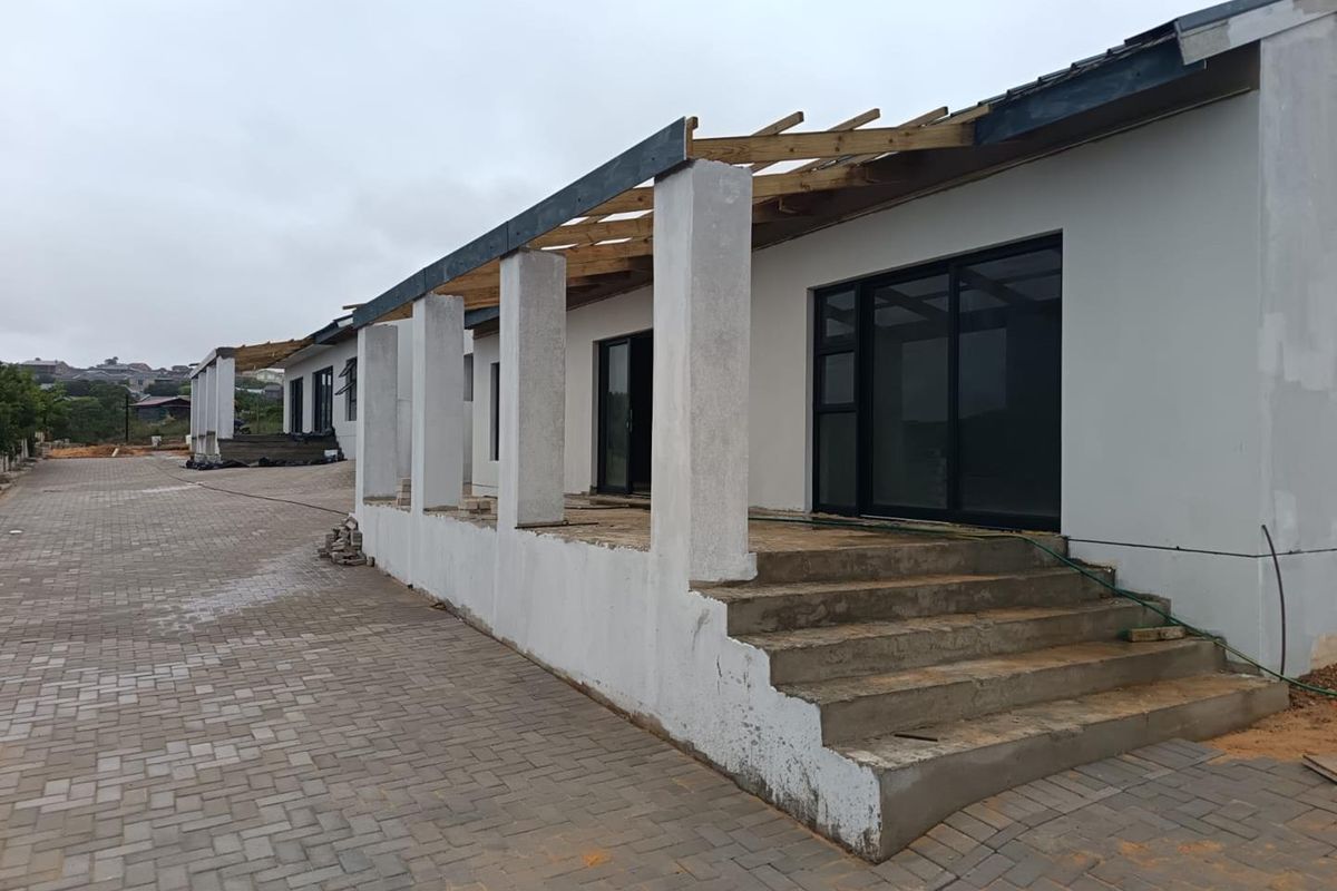 Exterior view of a house under construction, featuring a paved driveway, concrete stairs, and an unfinished patio roof structure.