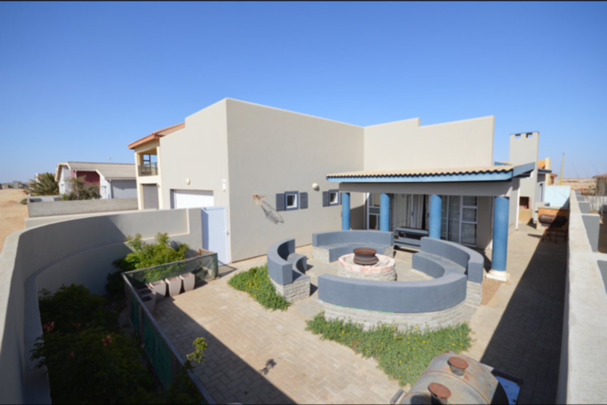 Rear exterior view featuring a paved courtyard, built-in circular seating area with fire pit, and a covered patio with structural columns.
