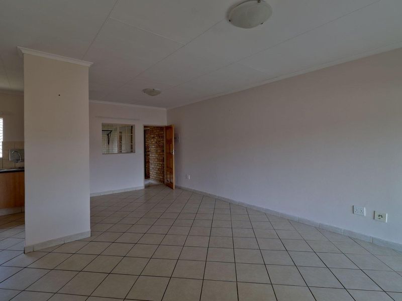 An empty open-plan living area featuring neutral tiled flooring, clean walls, and access to an adjacent kitchen space.