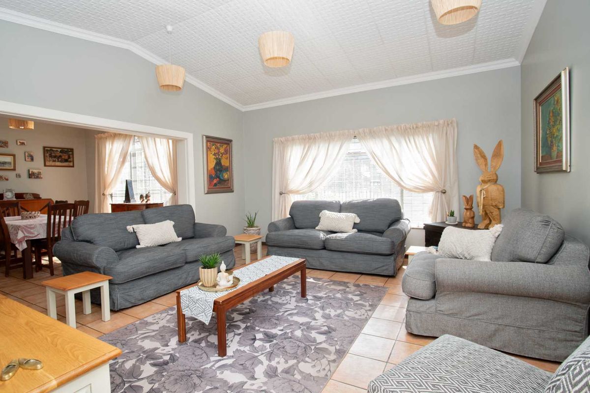 A spacious living room featuring tiled flooring and a textured ceiling, with an open-plan flow leading into the adjacent dining area.