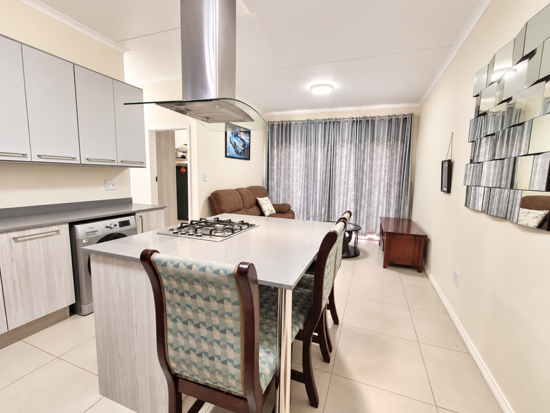Modern open-plan kitchen and living area featuring a central island with gas hob, sleek cabinetry, and neutral tiled flooring throughout.