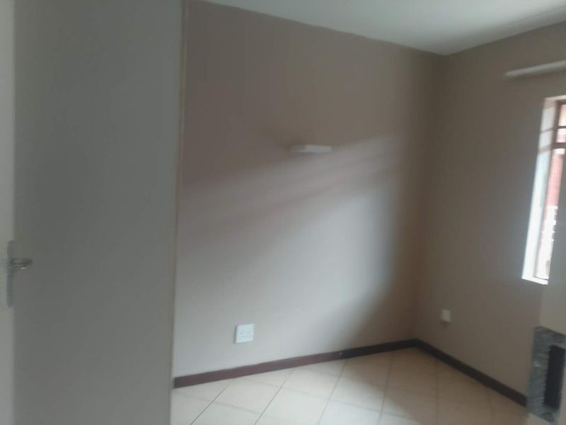 An empty bedroom featuring neutral wall paint, tiled flooring, and a wall-mounted light fixture.