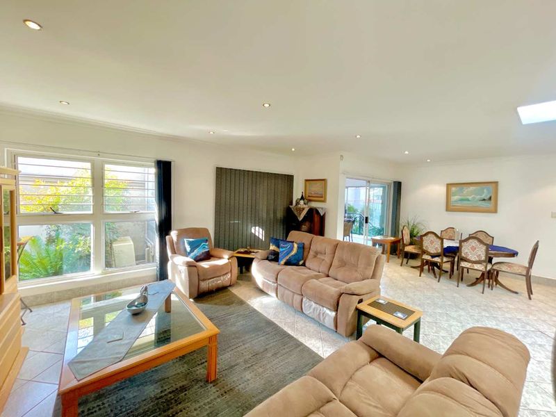 Spacious open-plan living and dining area featuring tiled flooring, recessed downlights, and large windows providing natural light and garden views.
