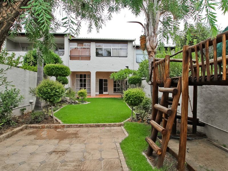 Rear view of the townhouse featuring a paved patio area, a well-maintained lawn, and a private garden space with access to the main dwelling.