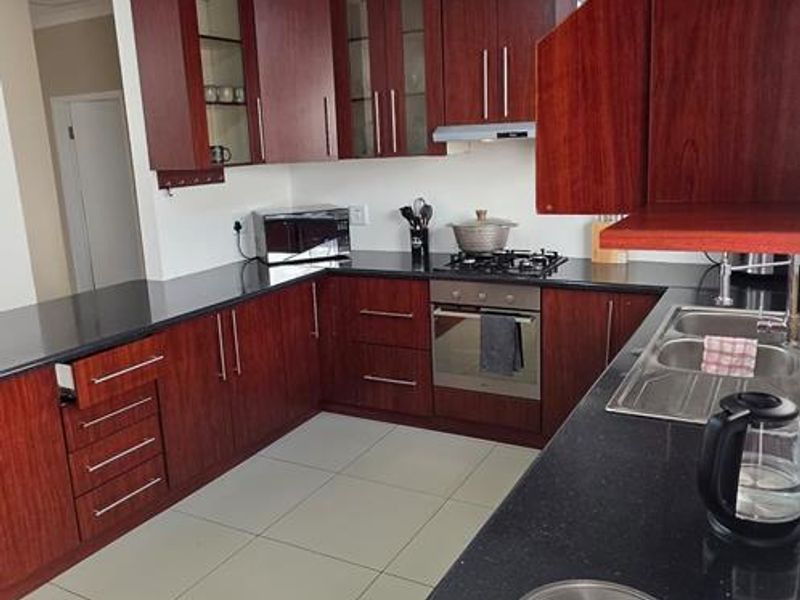 A functional kitchen featuring dark wood cabinetry, black granite countertops, built-in oven, gas hob, and tiled flooring.