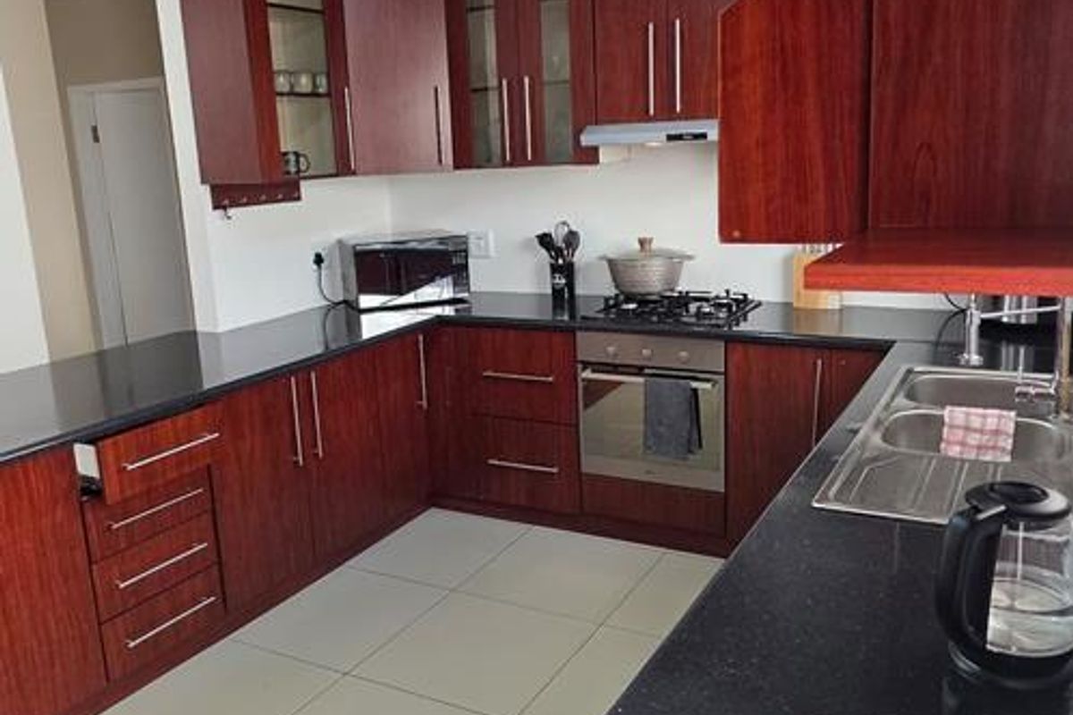 A functional kitchen featuring dark wood cabinetry, black granite countertops, built-in oven, gas hob, and tiled flooring.