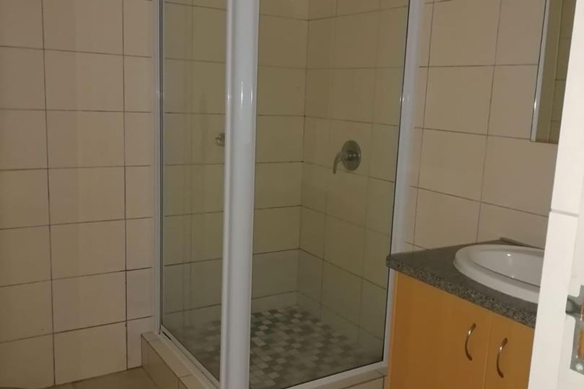 A functional bathroom featuring a corner shower enclosure, a vanity with a basin, and neutral wall and floor tiling.