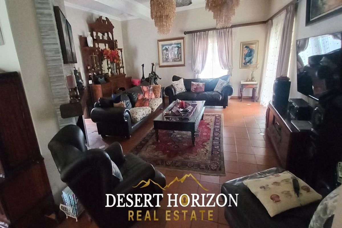 A spacious living room featuring tiled flooring, decorative ceiling cornices, and large windows allowing for natural light.
