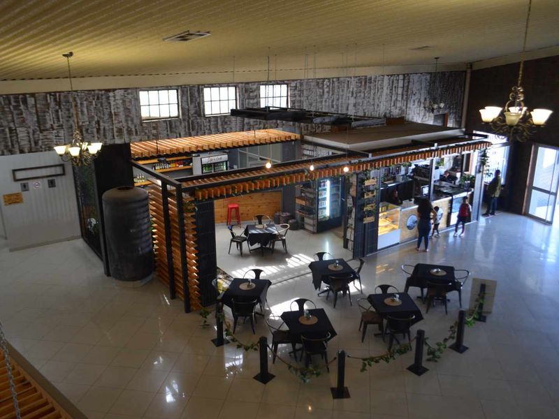 Spacious open-plan commercial area featuring tiled flooring, a central bar counter with timber slat detailing, and decorative chandeliers under a high suspended ceiling.