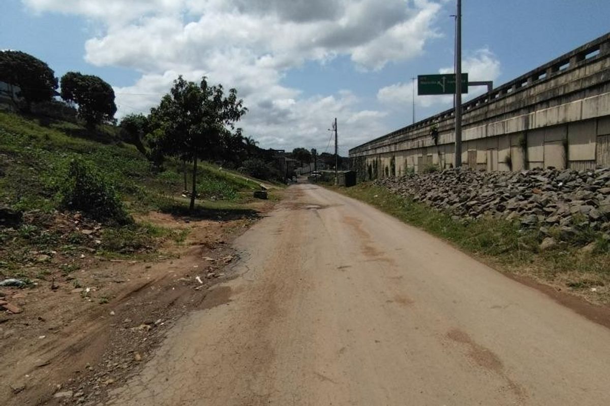 A view of an unpaved access road adjacent to a concrete retaining wall and highway infrastructure.