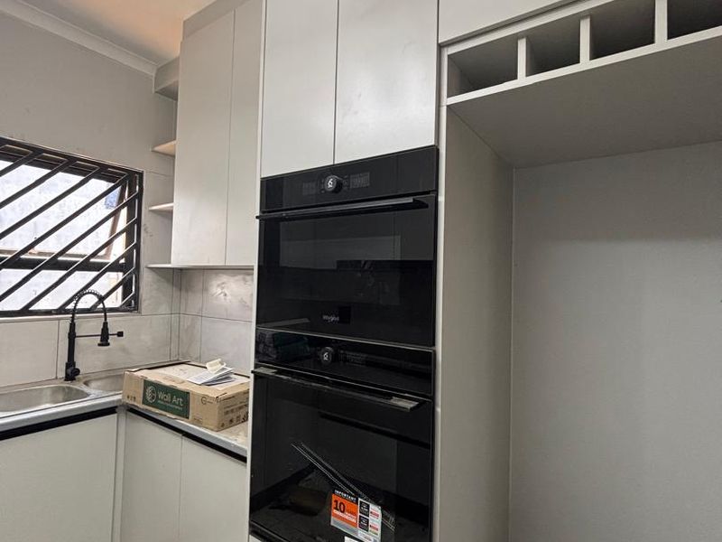 Modern kitchen featuring built-in oven and microwave, sleek cabinetry, and stainless steel sink, currently in a clean, near-finished state.