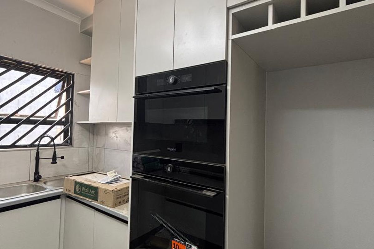 Modern kitchen featuring built-in oven and microwave, sleek cabinetry, and stainless steel sink, currently in a clean, near-finished state.