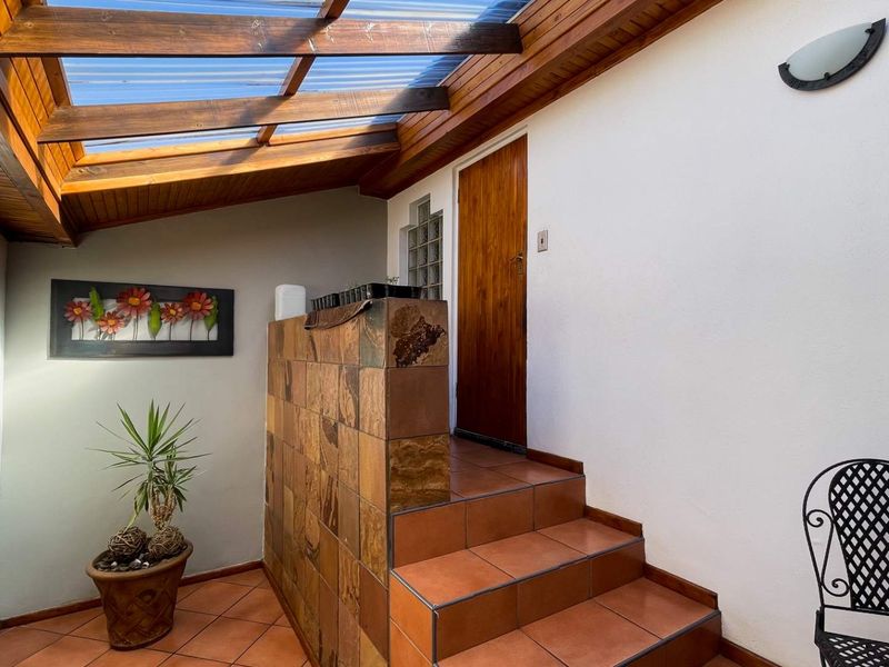 A covered patio area featuring a timber-framed roof, slate-tiled feature wall, and tiled staircase leading to an entrance.