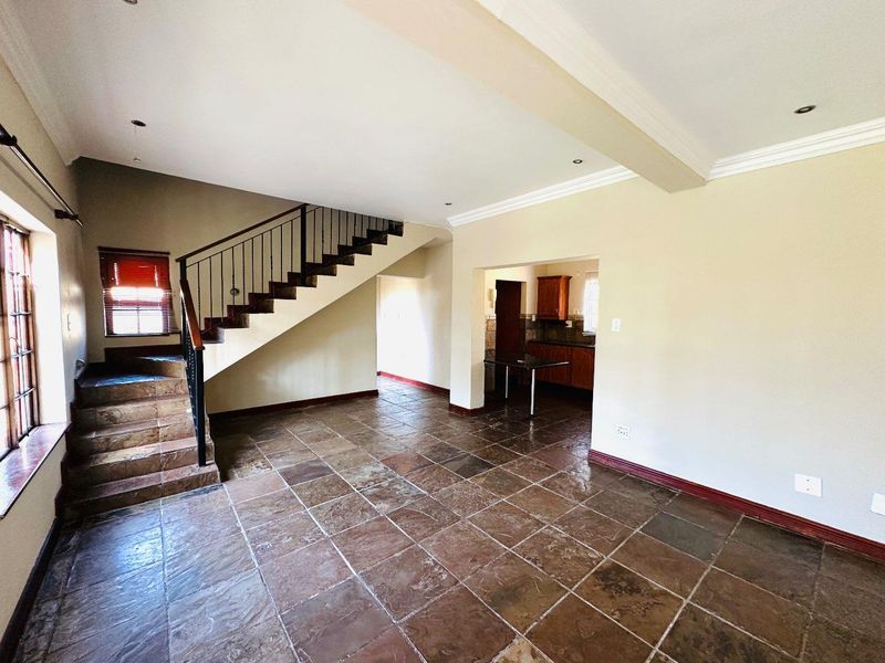 Spacious open-plan living area featuring stone tile flooring, a prominent staircase with metal balustrade, and a view into the adjacent kitchen space.