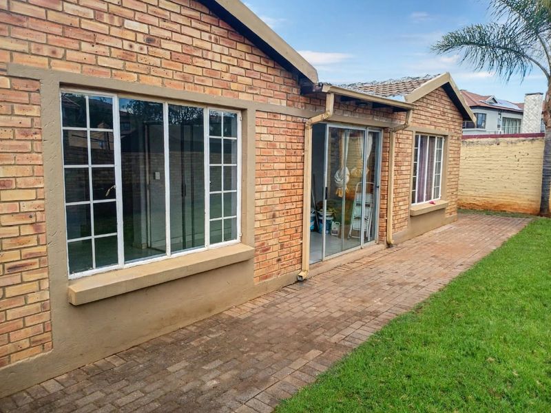Rear view of the townhouse featuring a face brick facade, paved patio area, and sliding glass doors leading into the living space.