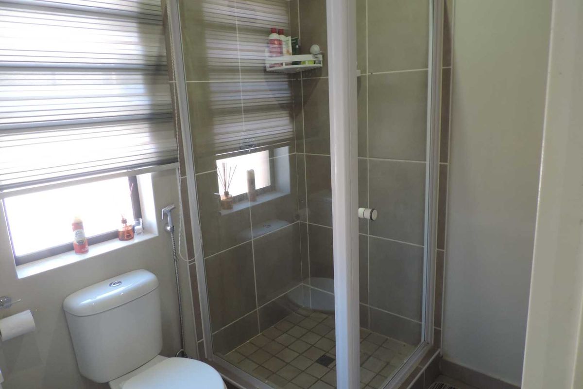 A functional bathroom featuring a glass-enclosed shower, tiled wall finishes, and a standard toilet, complemented by window blinds for privacy.