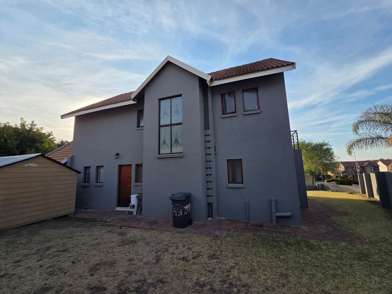 Rear view of a double-storey residential house featuring grey plastered walls, a tiled roof, and paved ground area.