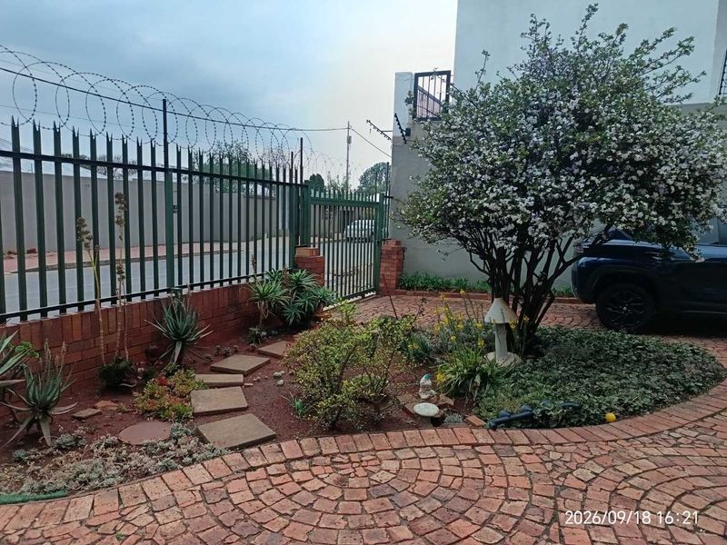Front entrance area featuring brick paving, landscaped garden beds, and secure perimeter fencing with razor wire.
