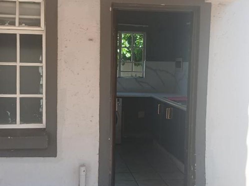 Exterior view of a rear entrance leading into a kitchen area, featuring cracked concrete flooring and visible wear on the exterior wall finishes.