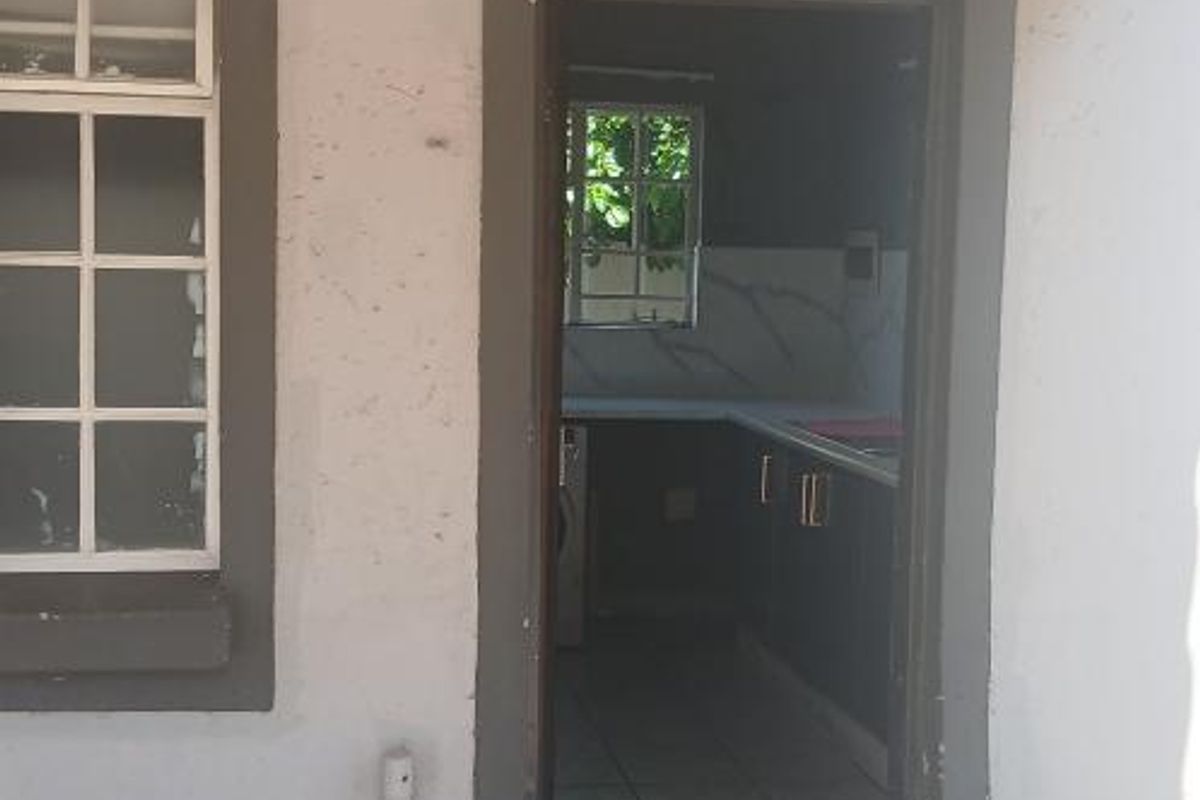 Exterior view of a rear entrance leading into a kitchen area, featuring cracked concrete flooring and visible wear on the exterior wall finishes.