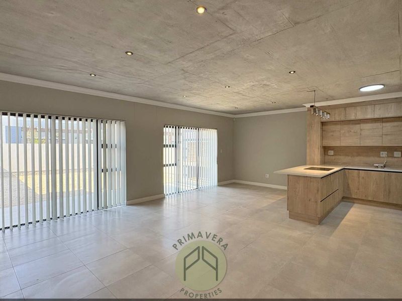 Spacious open-plan living and kitchen area featuring an exposed concrete ceiling, modern cabinetry, kitchen island, and large sliding doors leading to the garden.