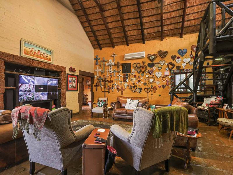 Spacious living room featuring a high thatched ceiling with exposed timber rafters, stone flooring, and a prominent stone fireplace.