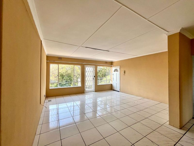 An empty, open-plan living area featuring tiled flooring, security gates, and large windows, offering a blank canvas for renovation and interior design.