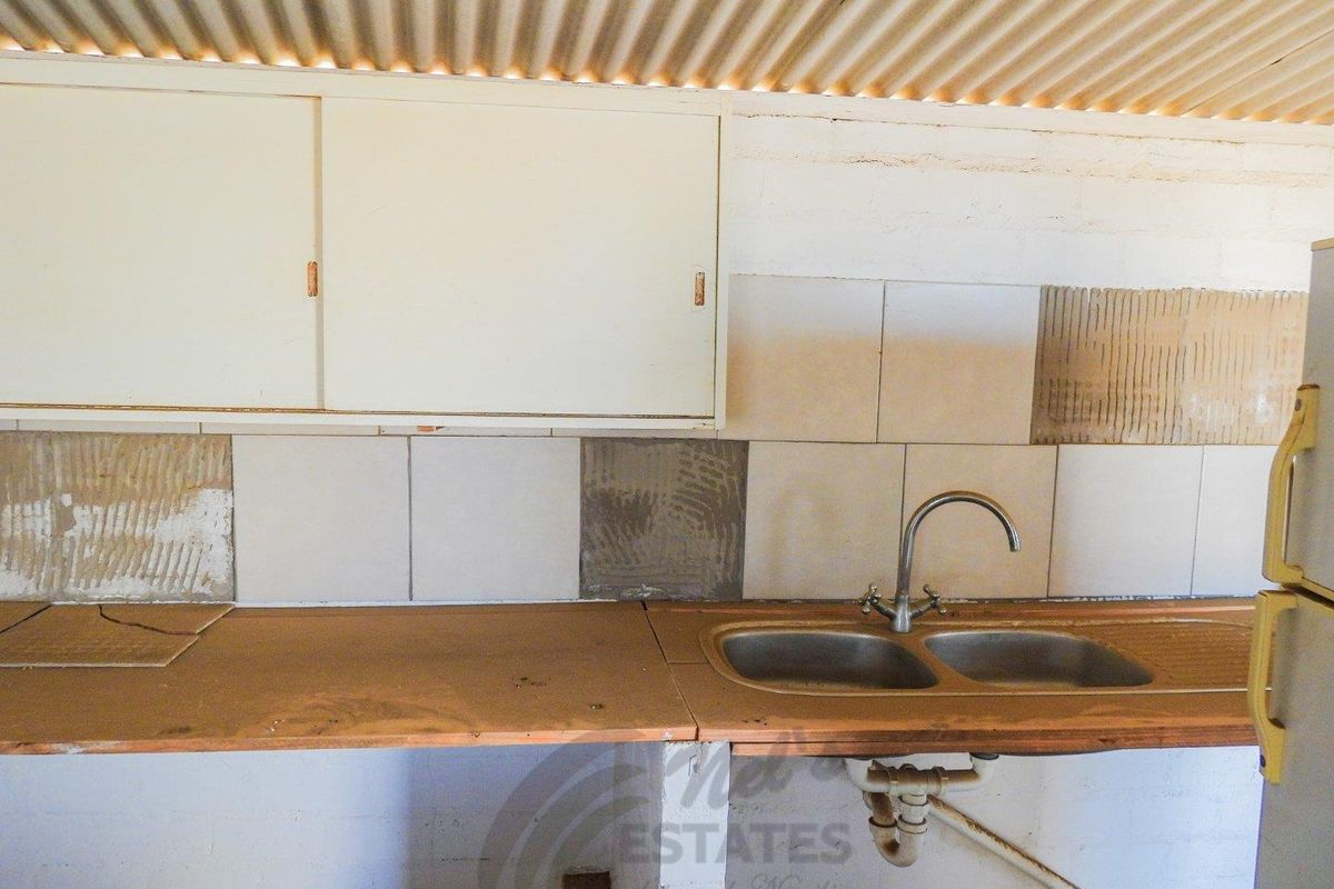 A basic kitchen area featuring a double stainless steel sink, wooden countertop, and wall-mounted cabinetry under a corrugated metal roof.