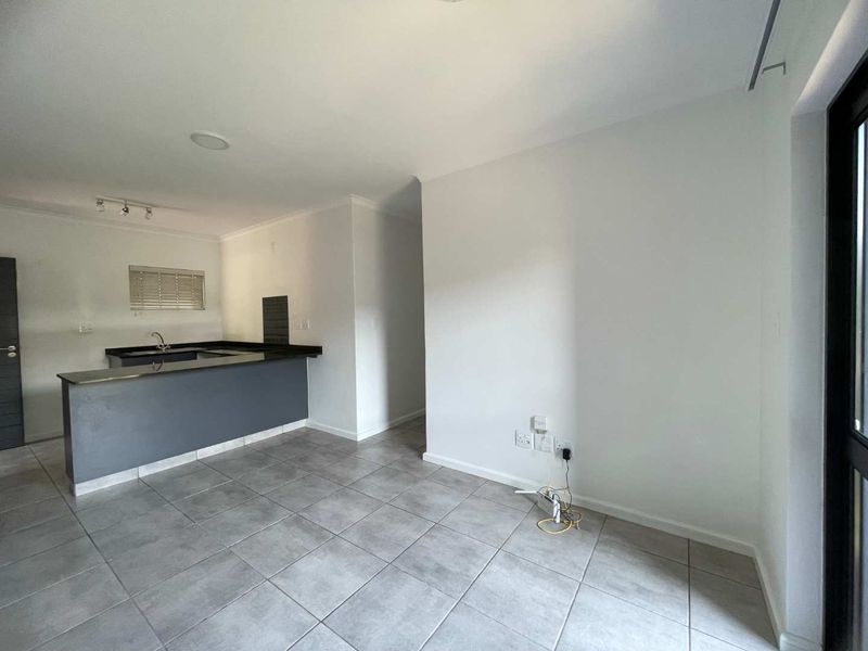 An open-plan living and kitchen area featuring neutral tiled flooring, a modern kitchen island, and clean, minimalist finishes throughout the space.