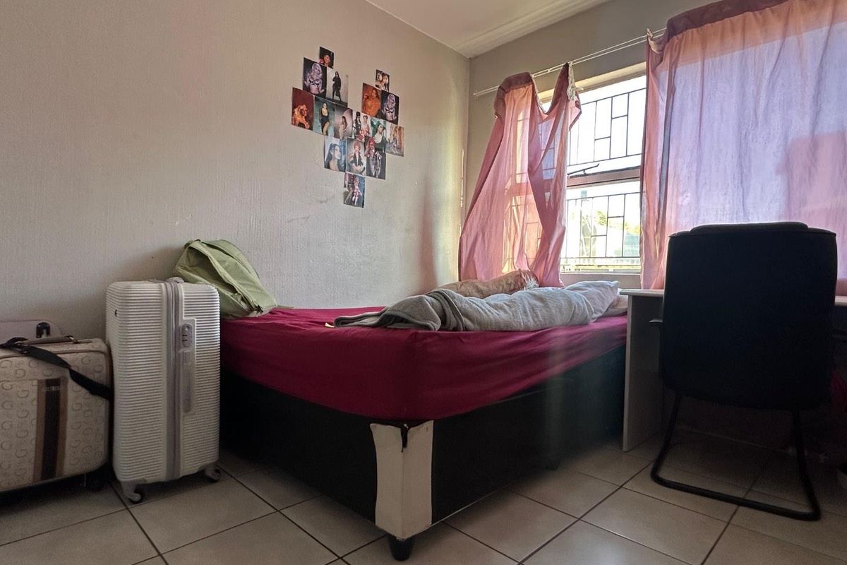 A compact bedroom featuring tiled flooring, a window with security bars, and neutral wall finishes.