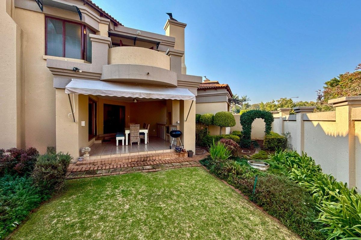Rear view of the property featuring a covered patio with a retractable awning, a balcony, and a well-maintained landscaped garden with boundary walls.