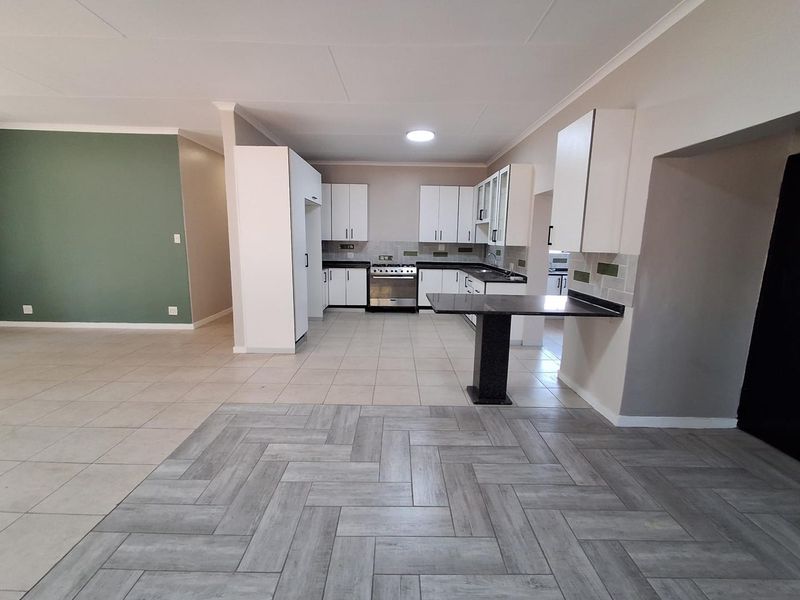 Spacious open-plan kitchen featuring white cabinetry, granite countertops, a gas stove, and a breakfast nook, seamlessly flowing into the living area.