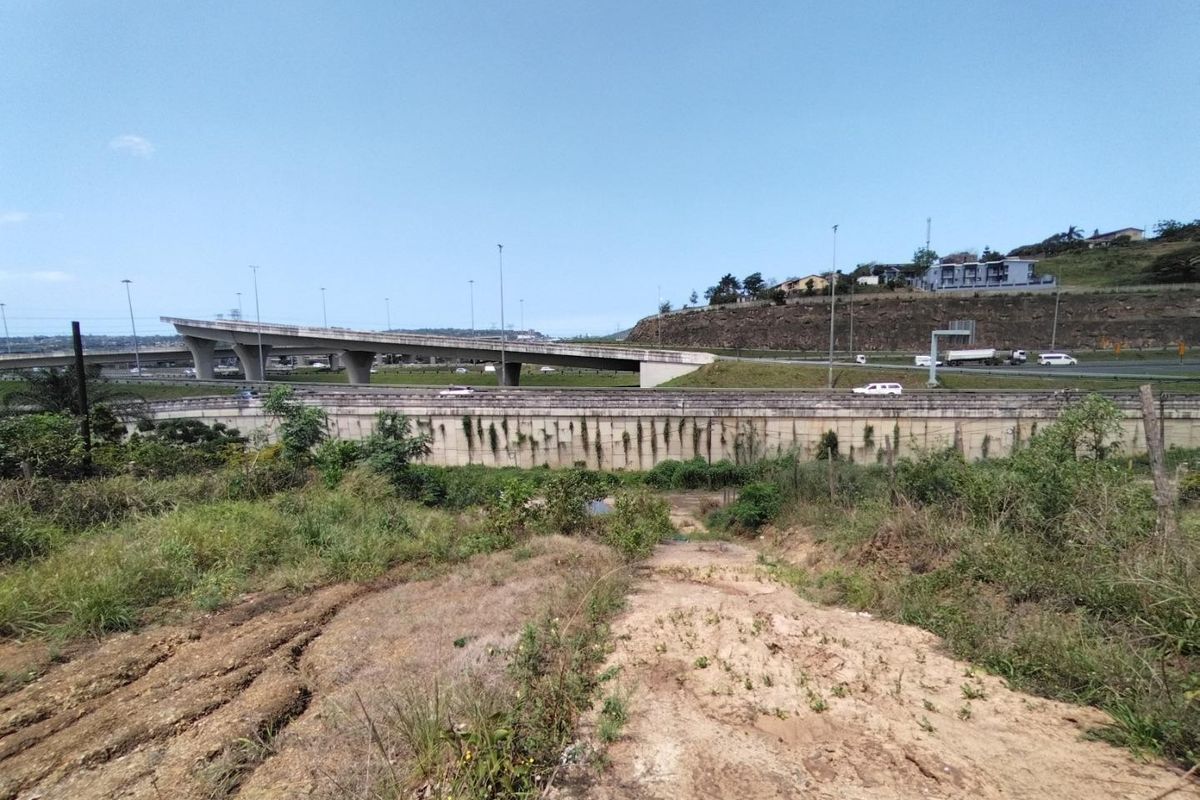 A view of the vacant land showing natural terrain with soil erosion, overlooking a nearby highway overpass and infrastructure.