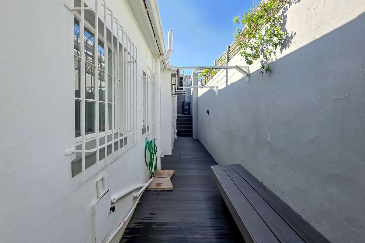 A narrow rear exterior walkway featuring timber decking, secure window bars, and a wall-mounted clothesline along the boundary wall.