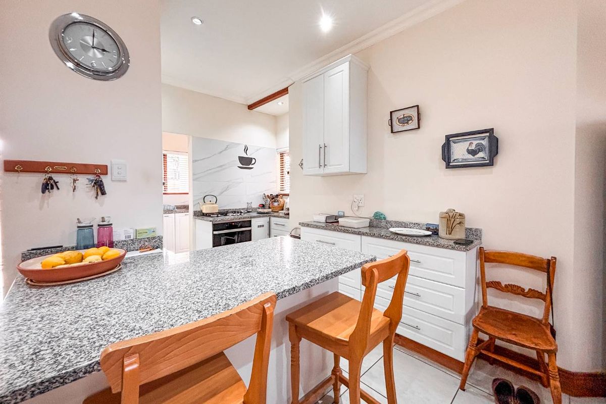A functional kitchen featuring granite countertops, white cabinetry, and a breakfast bar, with a separate scullery area visible in the background.