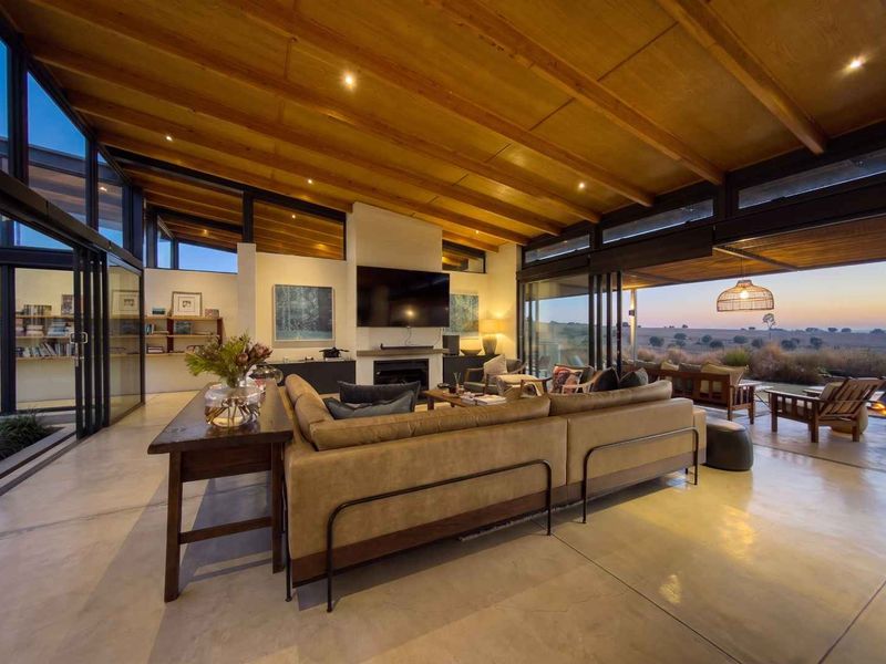 Spacious open-plan living area featuring polished concrete floors, exposed timber ceilings, and expansive glass sliding doors opening to a scenic outdoor patio.