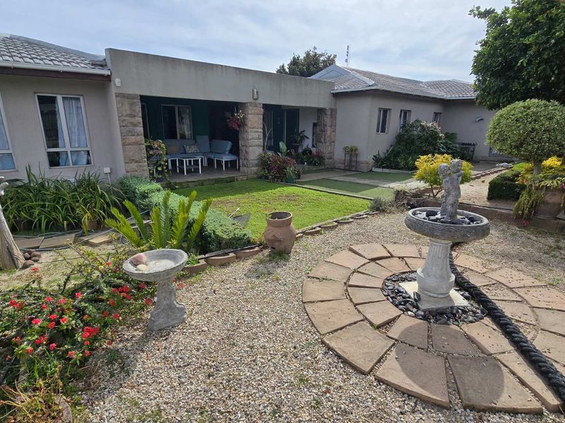 A rear view of the property featuring a covered patio with stone pillars, a landscaped garden, and a decorative stone water feature.