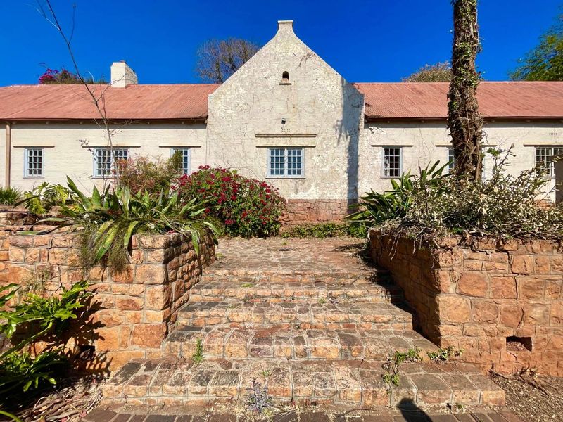 A historic-style residence featuring a stone staircase, retaining walls, and a corrugated metal roof, set within a mature garden landscape.