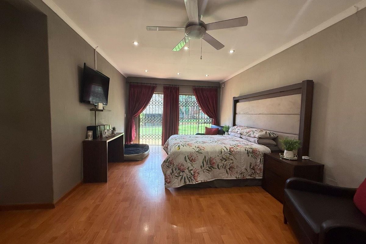 Spacious bedroom featuring laminate flooring, recessed ceiling lighting, a ceiling fan, and sliding glass doors with security gates leading to the garden.