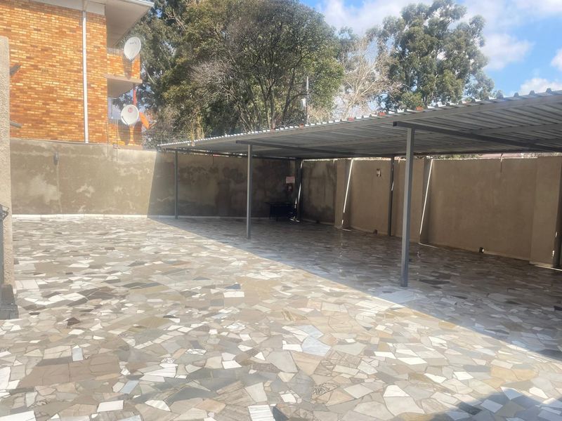A spacious outdoor carport area featuring paved flooring and a metal roof structure, enclosed by perimeter walls.