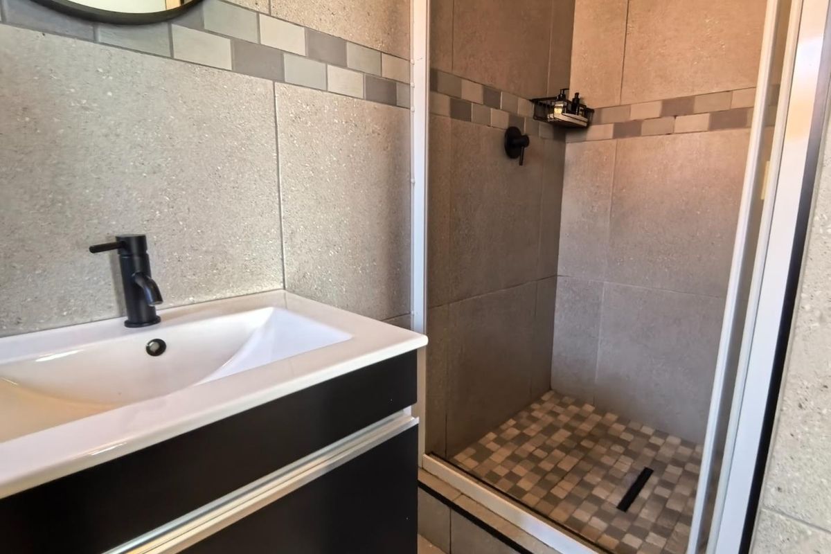 Modern bathroom featuring a vanity with basin, matte black mixer tap, and a tiled shower enclosure with a glass door.
