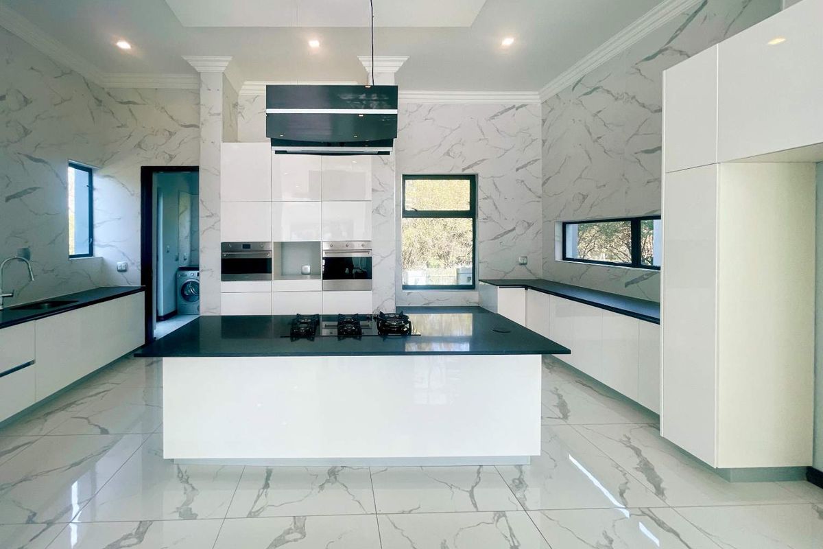 Modern kitchen featuring a central island with a built-in gas hob, sleek white cabinetry, marble-effect wall tiling, and integrated oven appliances.