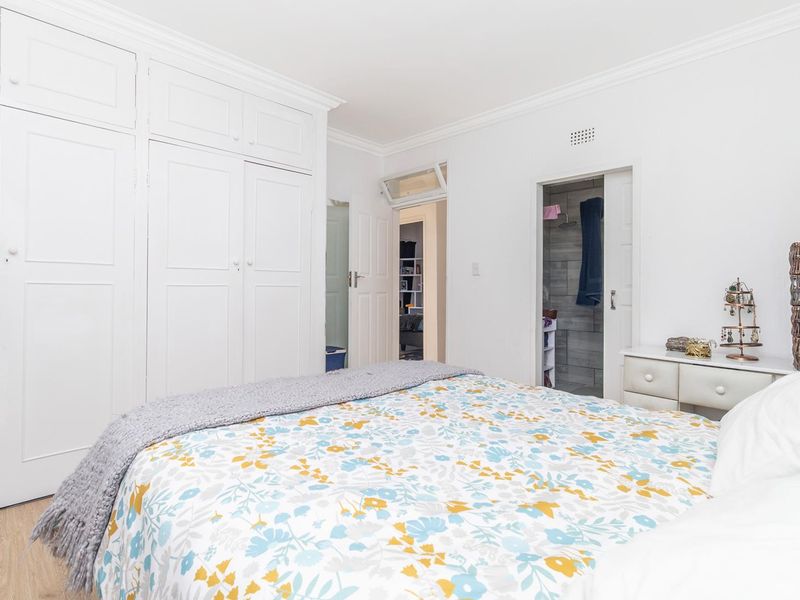 A bright bedroom featuring extensive built-in cupboards, crown molding, laminate flooring, and direct access to an en-suite bathroom.