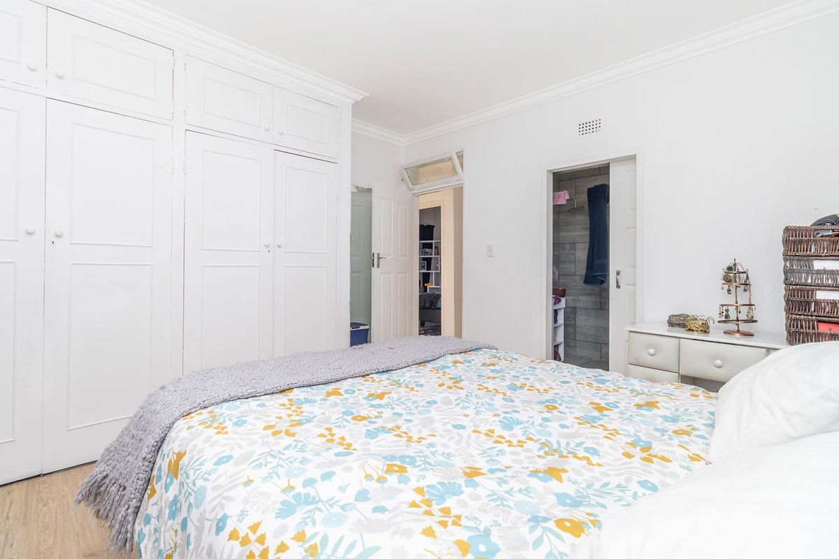 A bright bedroom featuring extensive built-in cupboards, crown molding, laminate flooring, and direct access to an en-suite bathroom.