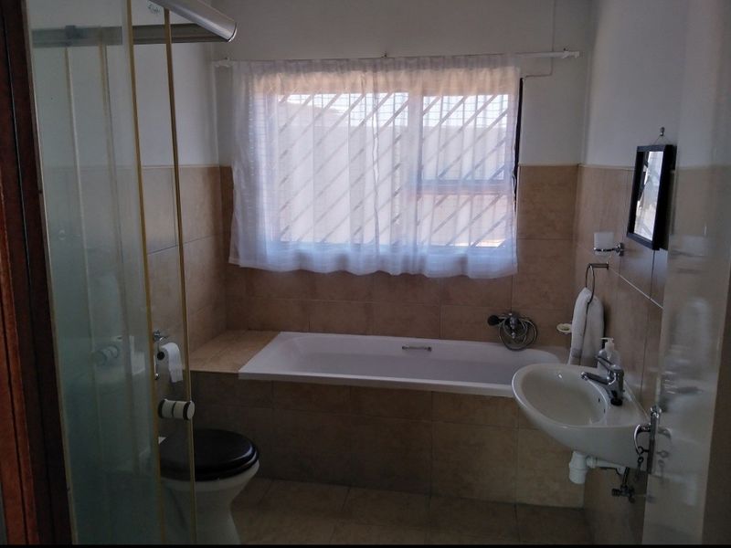 A functional bathroom featuring a built-in bathtub, wall-mounted basin, shower enclosure, and tiled finishes throughout.