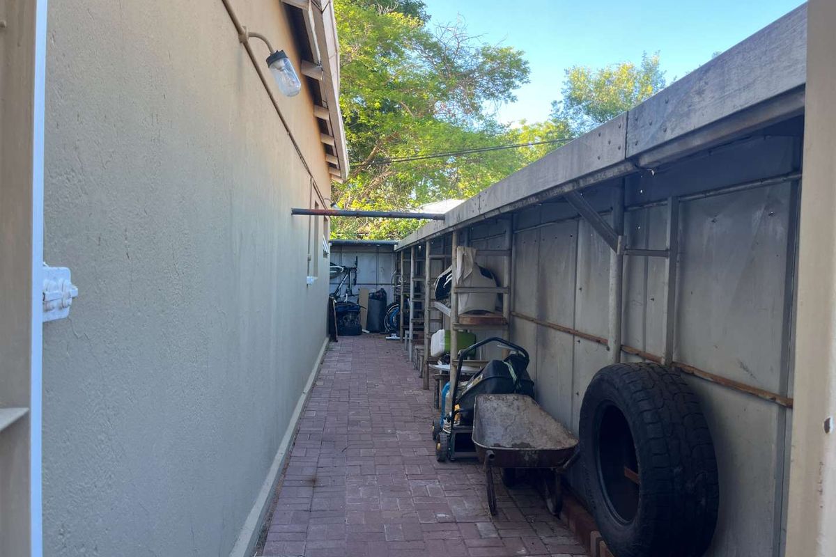 A narrow side passage featuring paved flooring and a long, built-in metal storage rack structure along the boundary wall.