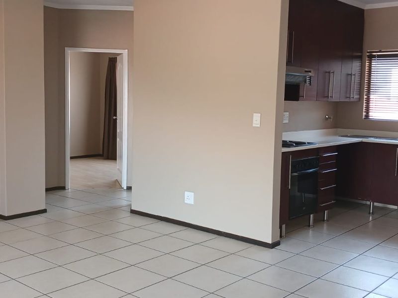 Open-plan living area featuring a functional kitchen with built-in cabinetry, oven, hob, and breakfast counter, finished with neutral tiled flooring throughout.